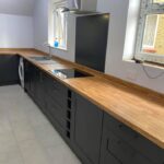 A black kitchen with wooden worktops and a sink.