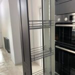 An empty metal pull-out pantry next to a built-in oven in a modern kitchen installation.