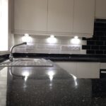 Modern kitchen installation interior with black countertops, white cabinets, and subway tile backsplash.