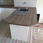 A modern kitchen installation with a wooden countertop island featuring a stainless steel sink, against a backdrop of tiled walls and a striped multicolored floor.