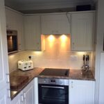 Modern kitchen interior with beige kitchen worktops, white cabinets, and stainless steel appliances.