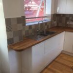 Modern kitchen corner with stainless steel sink, wooden kitchen worktop, and patterned backsplash.
