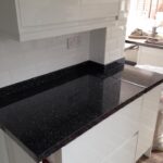Newly installed black granite kitchen worktop in a modern kitchen with white cabinets and subway tile backsplash.