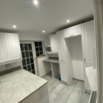 A well-lit, modern kitchen with white cabinets and gray kitchen worktops.