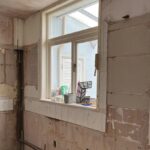 A partially demolished bathroom with exposed walls and plumbing, primed for a kitchen tiling makeover.