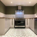 A modern kitchen installation with stainless steel appliances, white cabinetry, and patterned floor tiles.