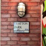 Wall-mounted light fixture above a 'Fratton Park' street sign on a kitchen tiling wall.