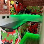 Home kitchen area with vibrant graffiti-style wall art, green under-cabinet lighting, and expert kitchen installation.