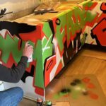 An artist is spray painting a colorful graffiti piece on a kitchen installation.