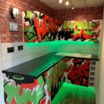 A vibrant urban-style kitchenette with graffiti wall art and green kitchen worktops.