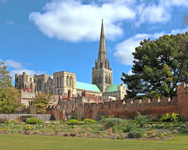 A majestic cathedral with a tall spire overlooks a serene walled garden under a clear blue sky, inspiring the latest in kitchen design.