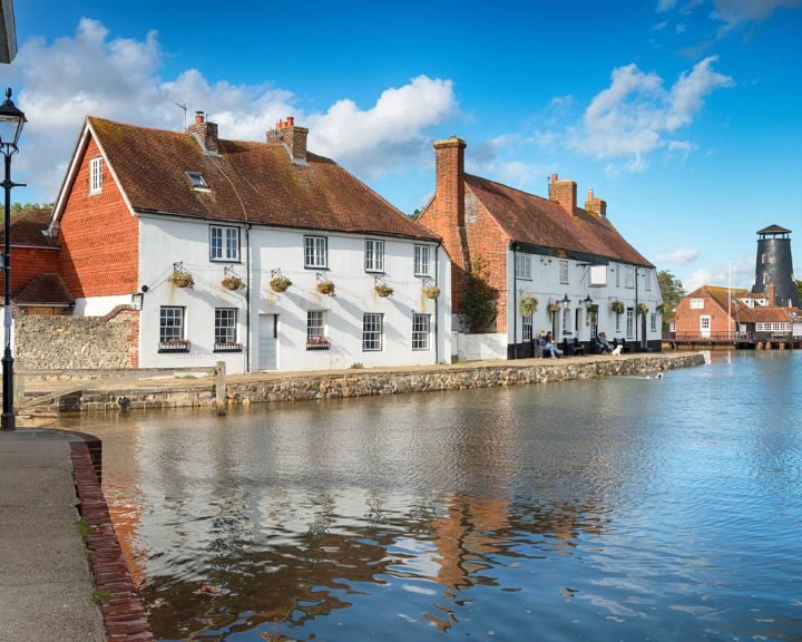 Quaint riverside houses with red-tiled roofs beside calm waters on a sunny day with blue skies, featuring kitchen tiling that complements their exterior charm.