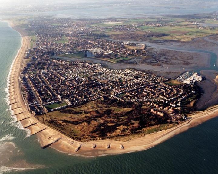 Aerial view of a coastal town with a curved sea wall and adjacent beach leading into a densely populated neighborhood, featuring detailed kitchen design.