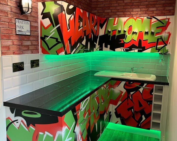 A vibrant kitchen with graffiti-style wall art and green illuminated countertops.