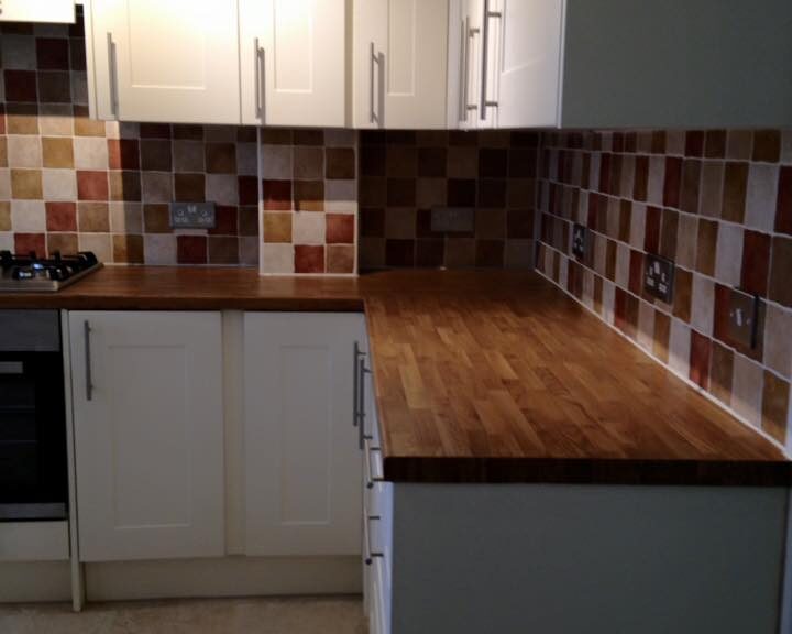 A modern kitchen design with white cabinets, brown tiled backsplash, and wooden worktops.