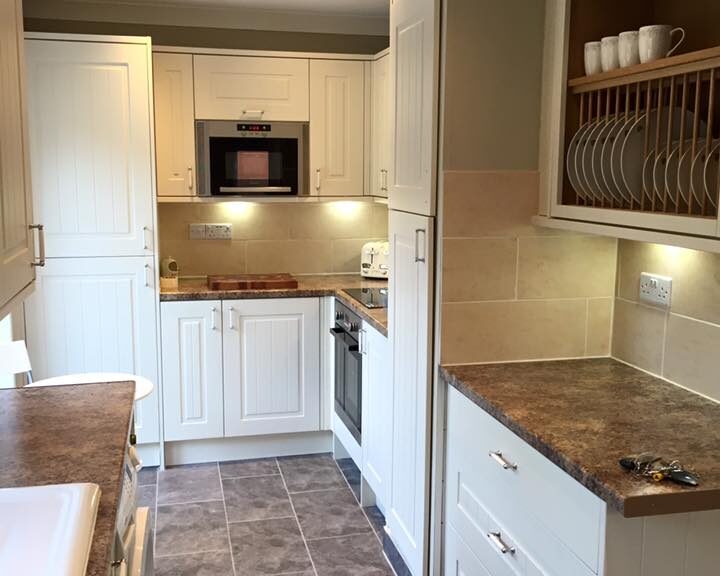 A modern kitchen installation with white cabinetry, stainless steel appliances, and a tile floor.