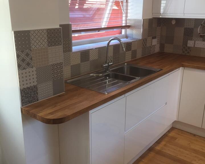 Modern kitchen corner with stainless steel sink, wooden kitchen worktop, and patterned backsplash.