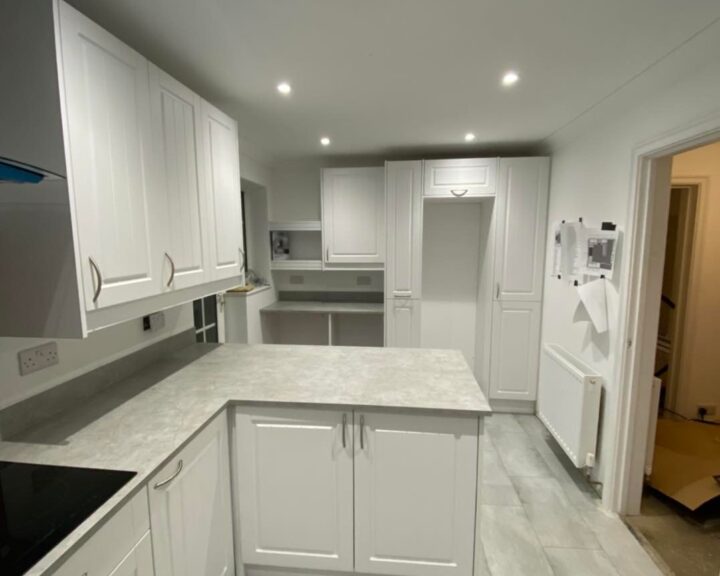 A modern kitchen with white cabinetry, gray kitchen worktop, and recessed lighting.