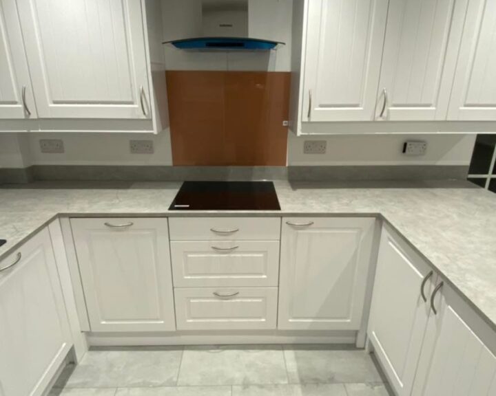 A modern kitchen with white cabinetry and a central island with a cooktop, featuring elegant kitchen tiling.