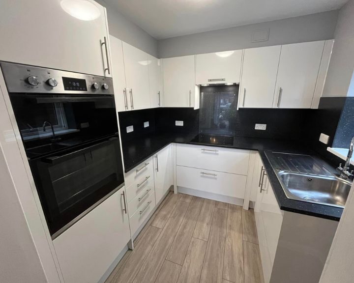 A modern kitchen with white cabinetry, black countertops, stainless steel appliances, and new kitchen tiling.