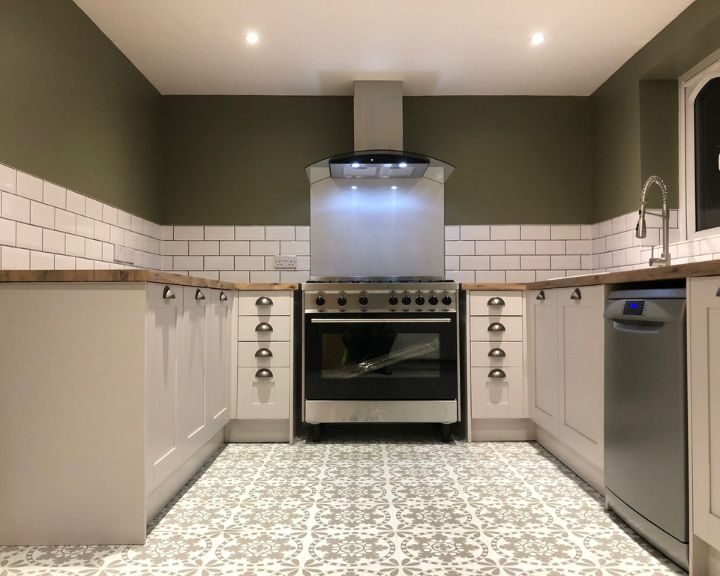 A modern kitchen installation with white cabinetry, stainless steel appliances, patterned floor tiles, and a range hood over a stove.