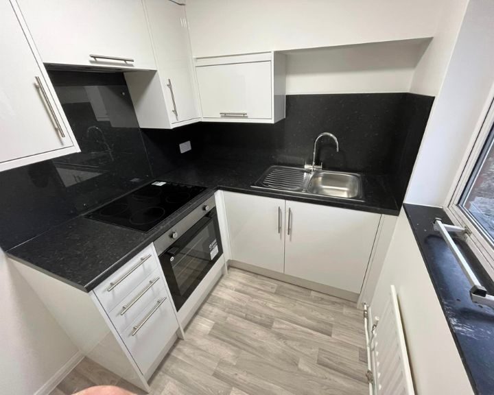 Modern kitchen design with white cabinetry, black countertops, and stainless steel appliances.