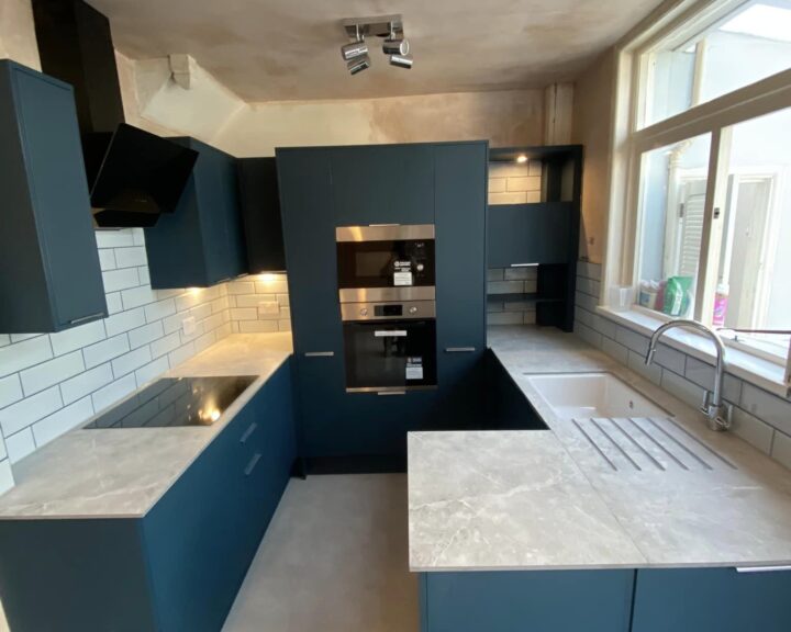 Modern kitchen installation with dark blue cabinets, white subway tile backsplash, and built-in appliances.