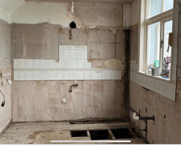 A room undergoing renovation for a new kitchen design, with stripped walls and exposed plumbing.