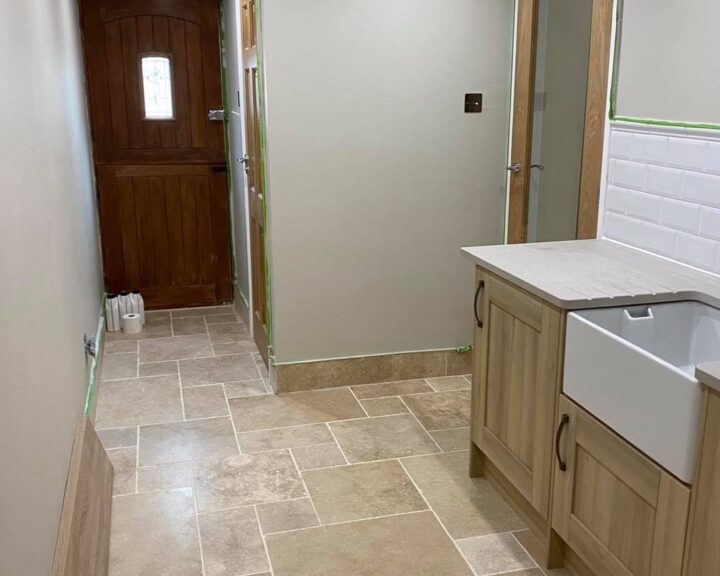 A newly renovated bathroom featuring beige floor tiles, a wood-finished vanity with a white kitchen worktop, and a partial view of a wooden door.