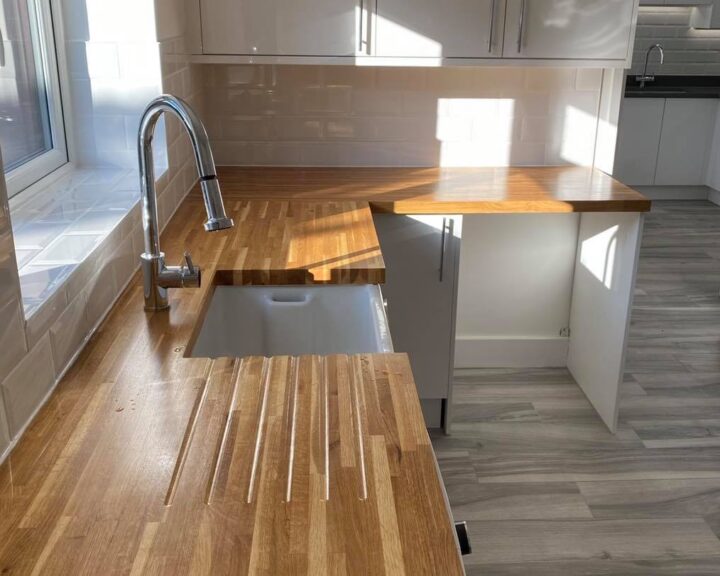 Modern kitchen with wooden countertops, a white undermount sink, stainless steel faucet, and kitchen tiling, bathed in natural sunlight.