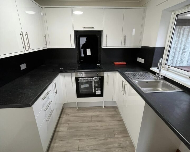 A modern kitchen design with white cabinets, black countertops, stainless steel appliances, and a wooden floor.