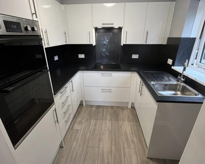 A modern kitchen design with white cabinetry, black countertops, and stainless steel appliances.