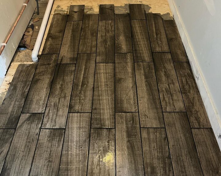Installation of dark wooden flooring in the kitchen design, with some areas incomplete, exposing underlayment and pipes.