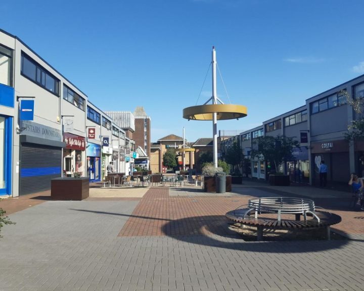 Sunny shopping street with benches and shops.
